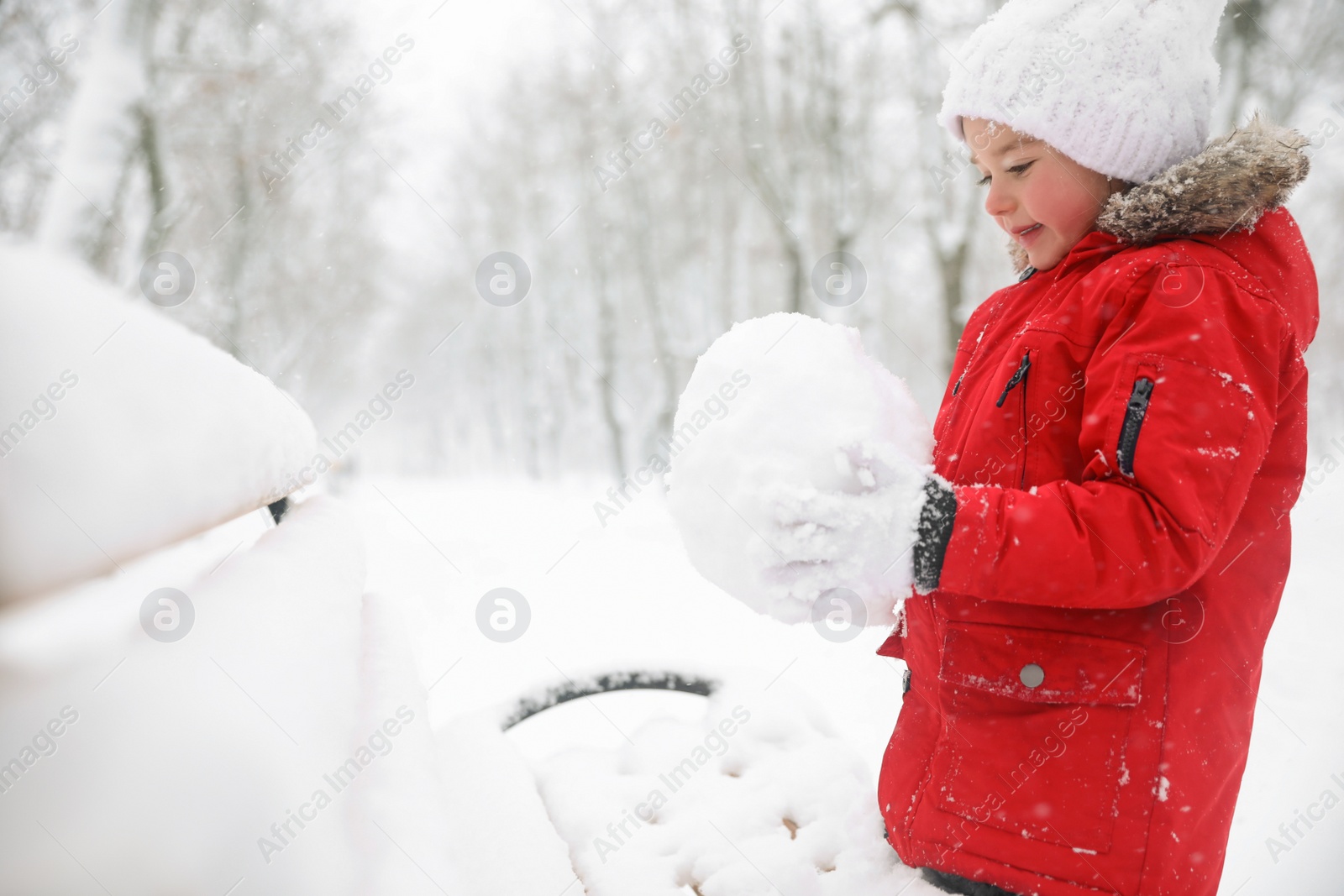 Photo of Cute little girl holding snowball near bench on winter day, space for text