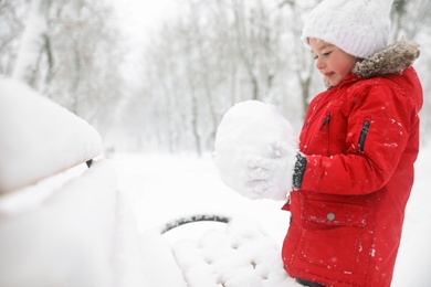 Photo of Cute little girl holding snowball near bench on winter day, space for text