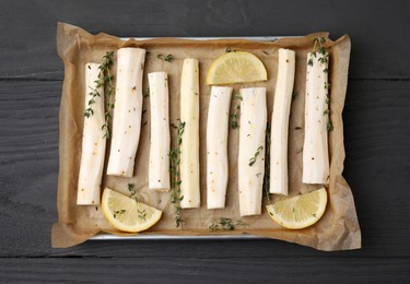 Photo of Baking tray with raw salsify roots, lemon and thyme on grey wooden table, top view