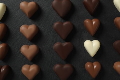 Beautiful heart shaped chocolate candies on black table, flat lay