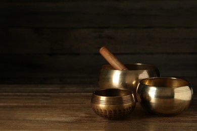 Golden singing bowls and mallet on wooden table, space for text