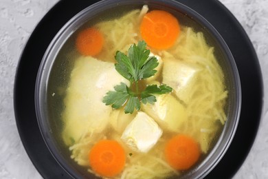 Photo of Tasty chicken soup with noodles, carrot and parsley in bowl on light textured table, top view