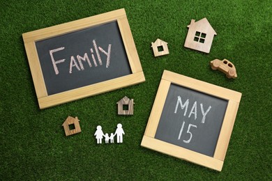 Photo of Chalkboards and wooden figures on green grass, flat lay. International Family Day