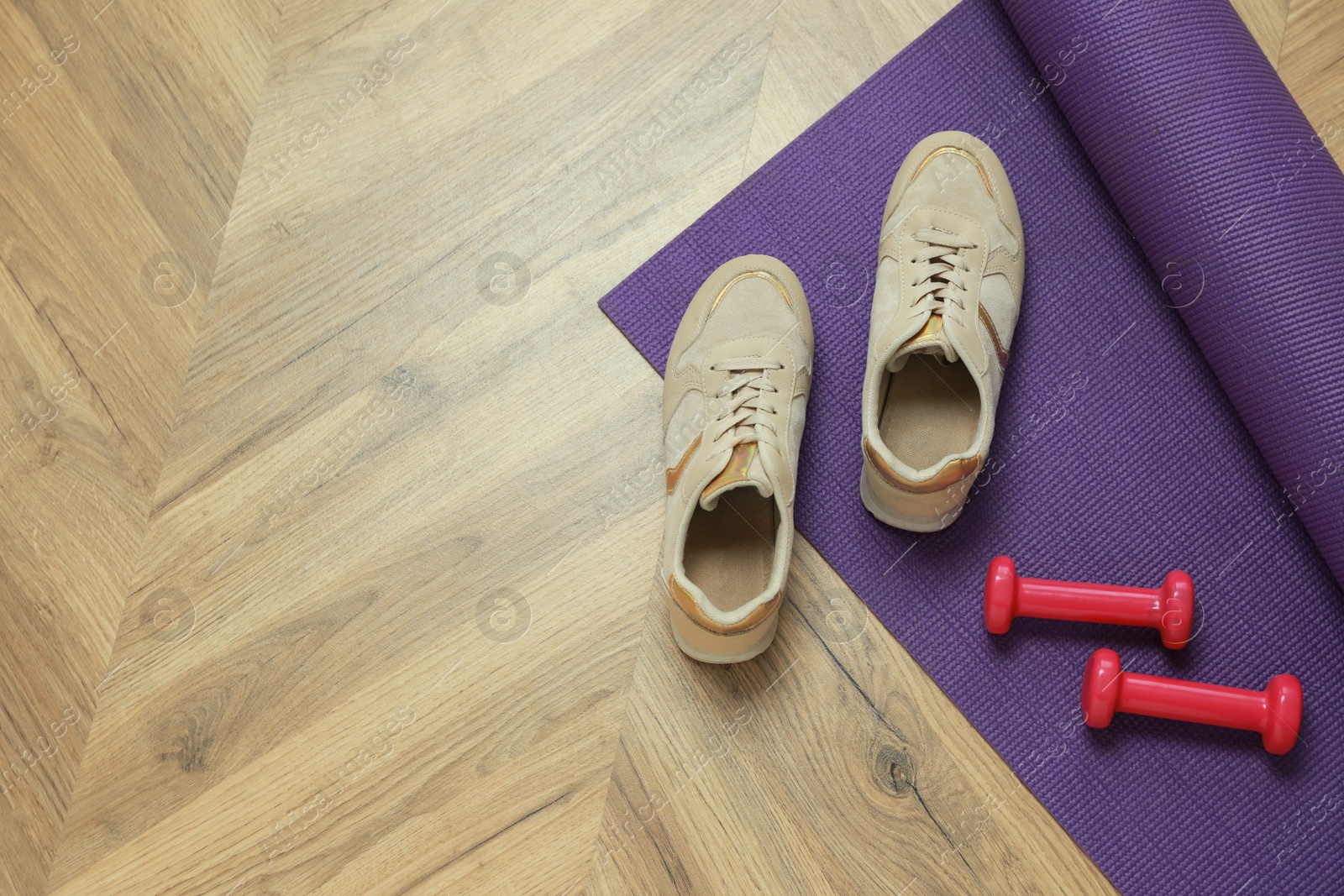 Photo of Dumbbells, sneakers and mat on wooden floor, above view. Space for text