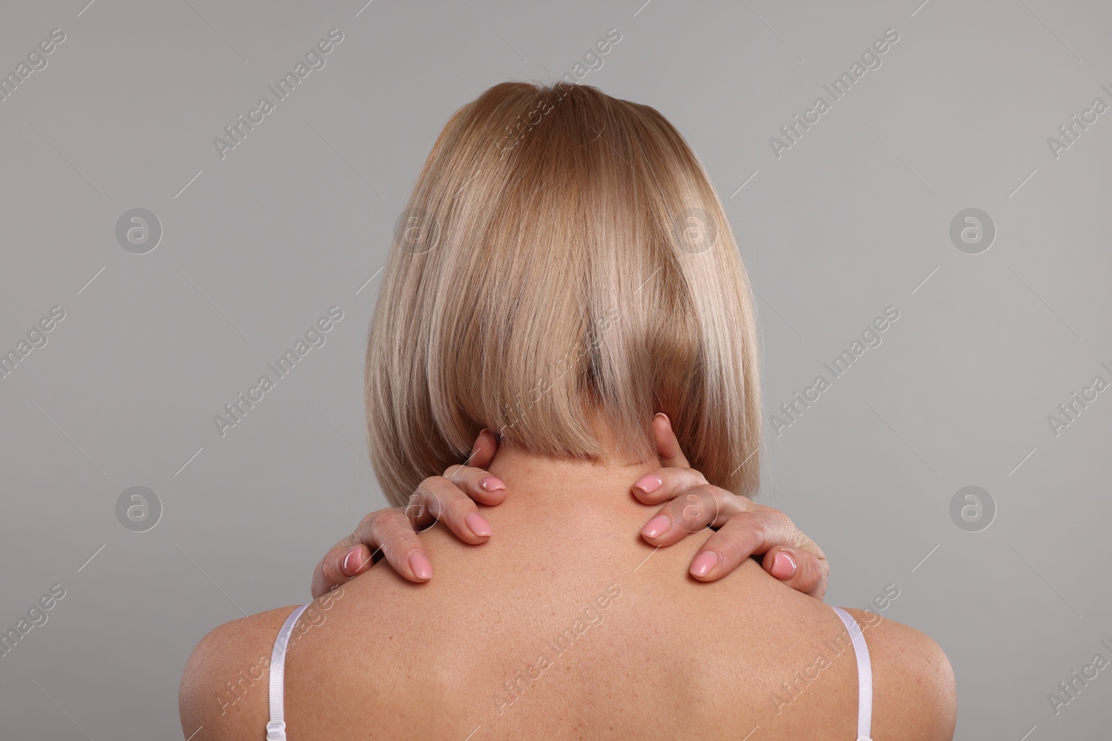 Photo of Woman suffering from pain in her neck on grey background, back view