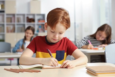 Photo of Cute little boy studying in classroom at school