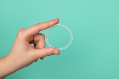 Photo of Woman holding diaphragm vaginal contraceptive ring on turquoise background, closeup. Space for text
