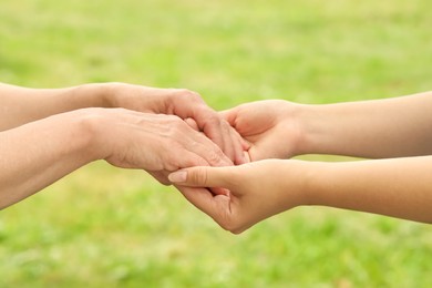 Photo of Young and elderly women holding hands outdoors, closeup