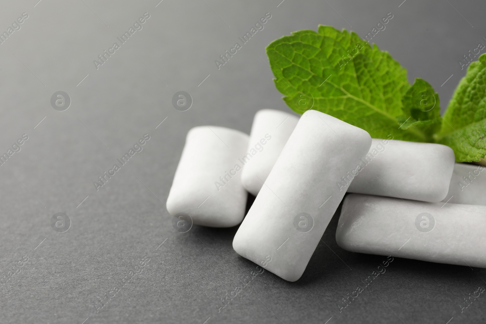 Photo of Tasty white chewing gums and mint leaves on grey background, closeup. Space for text
