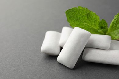 Tasty white chewing gums and mint leaves on grey background, closeup. Space for text