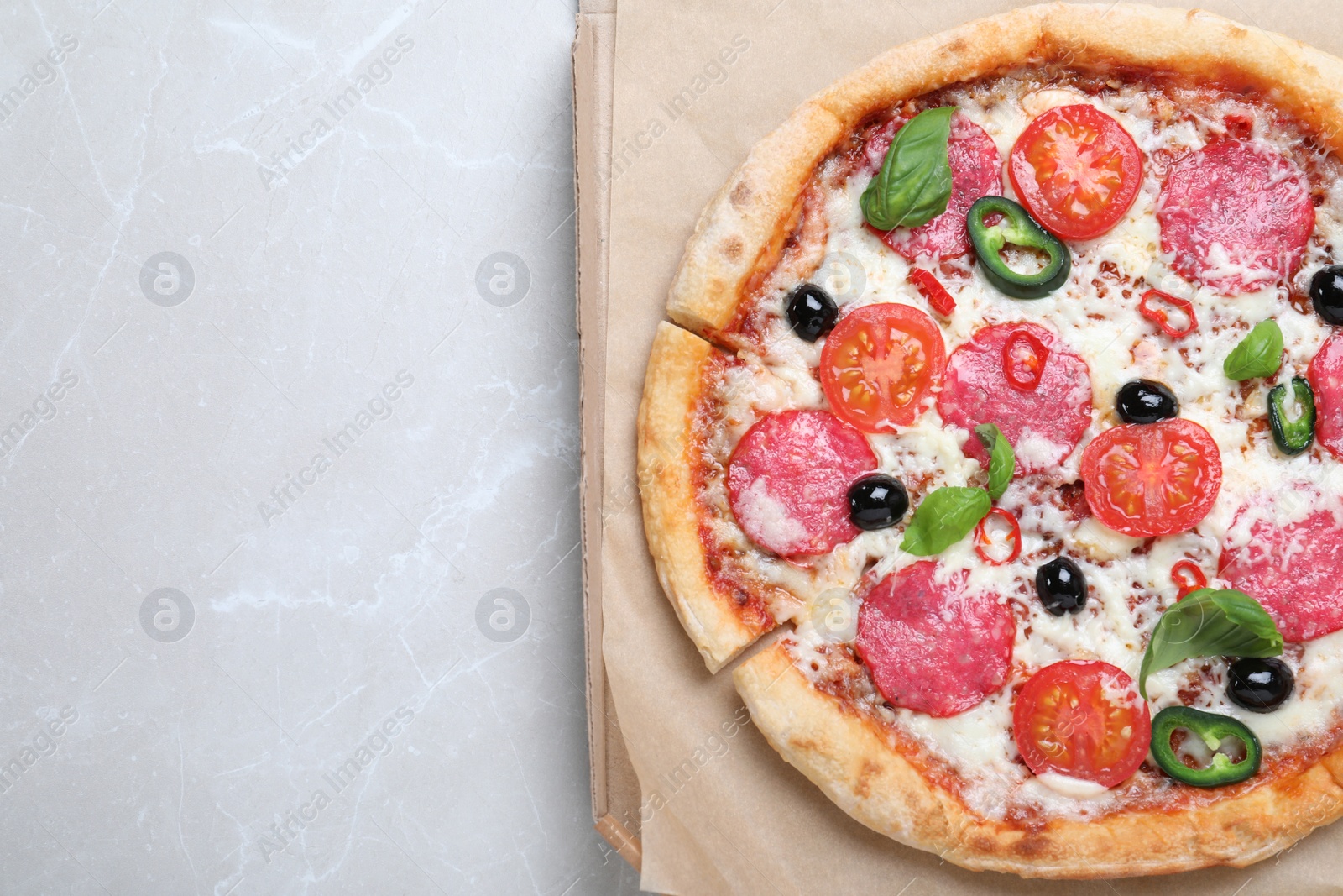 Photo of Delicious pizza Diablo in cardboard box on light marble background, top view. Space for text