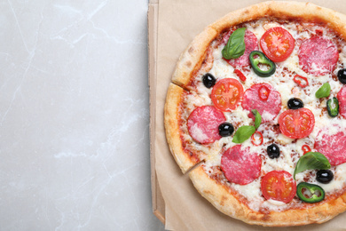 Photo of Delicious pizza Diablo in cardboard box on light marble background, top view. Space for text