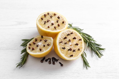 Photo of Lemons with cloves and fresh rosemary on white wooden table. Natural homemade repellent
