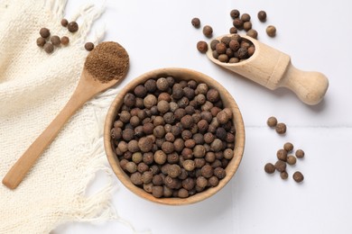 Photo of Ground and whole allspice berries (Jamaica pepper) on white tiled table, flat lay