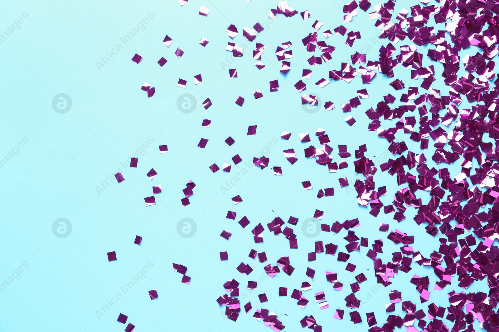 Photo of Shiny purple confetti on light blue background, flat lay