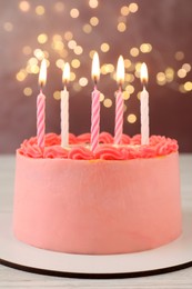 Cute bento cake with tasty cream and burning candles on white wooden table