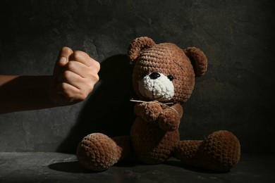 Photo of Stop child abuse. Man showing fist to toy bear in dark room, closeup