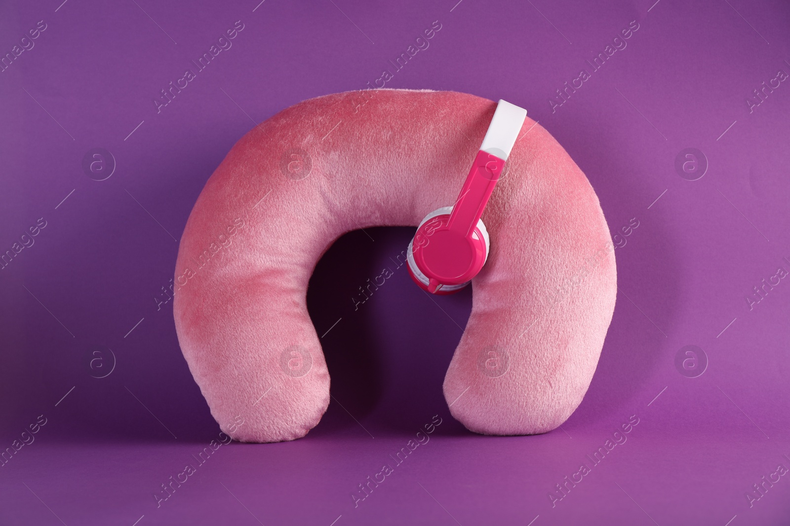 Photo of Pink travel pillow and headphones on violet background