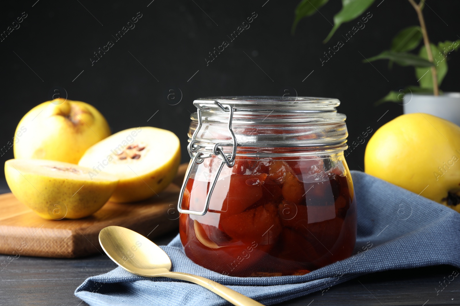 Photo of Quince jam in glass jar, spoon and fresh raw fruits on grey table, closeup