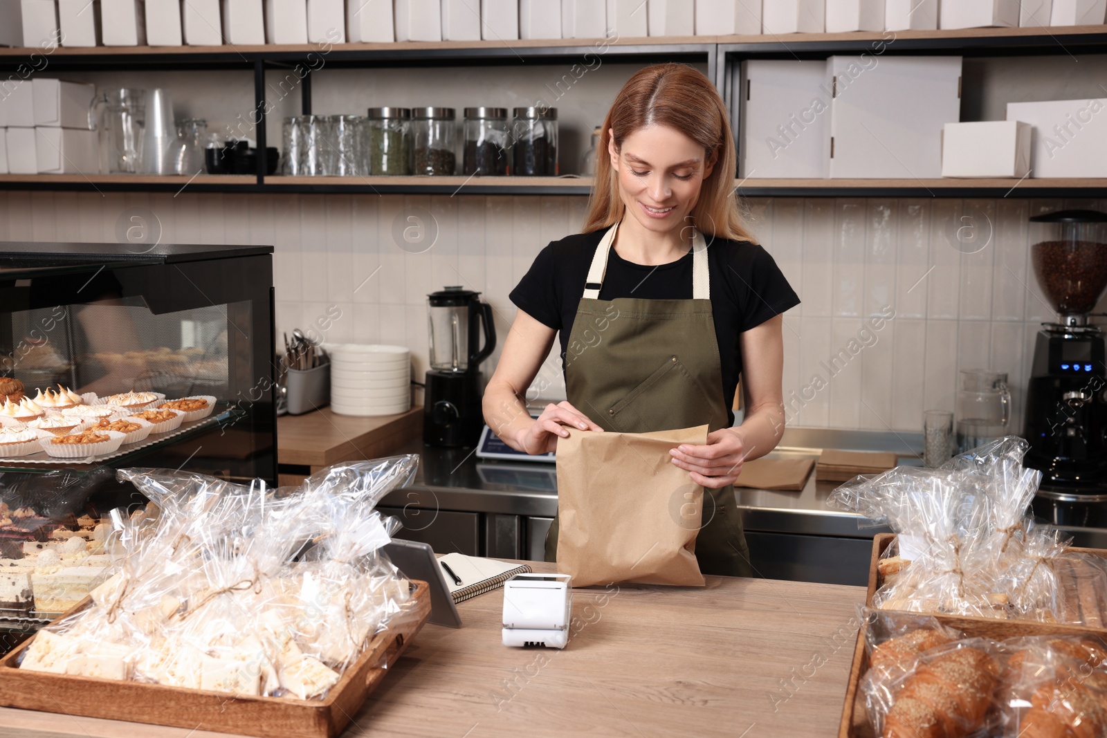 Photo of Happy seller with paper bag at cashier desk in bakery shop