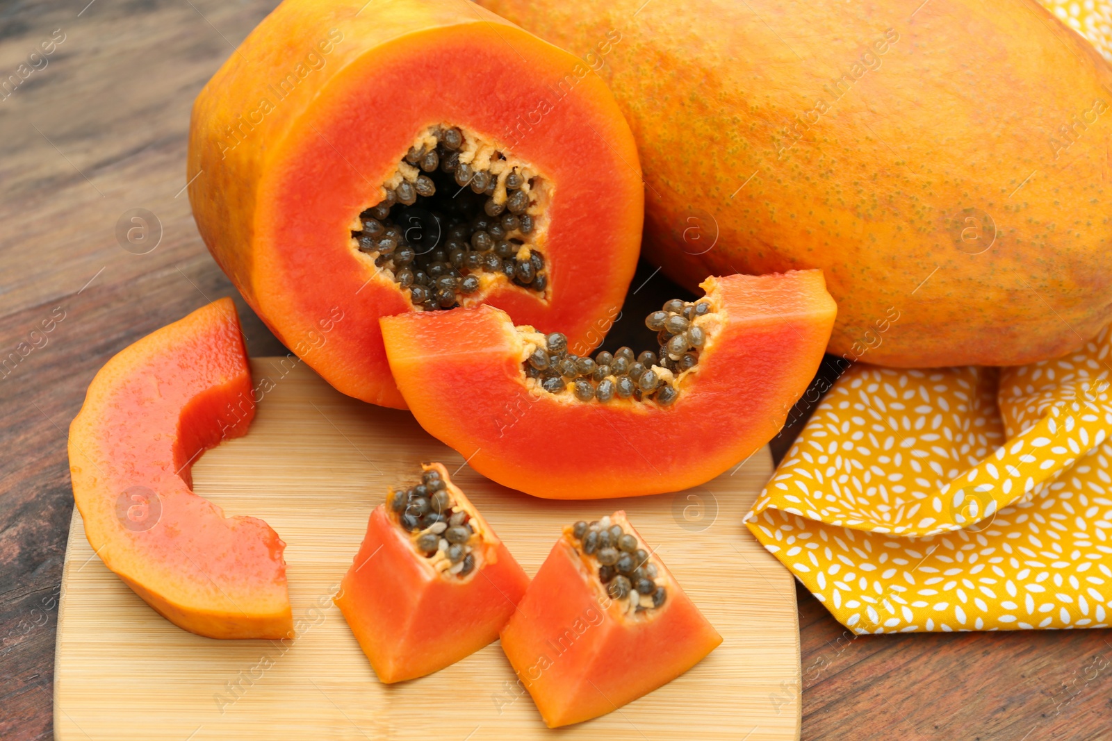 Photo of Ripe cut and whole papaya fruits on wooden table, closeup