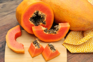 Ripe cut and whole papaya fruits on wooden table, closeup