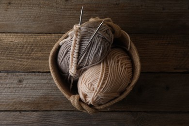 Soft colorful yarns, knitting and metal needles on wooden table, top view