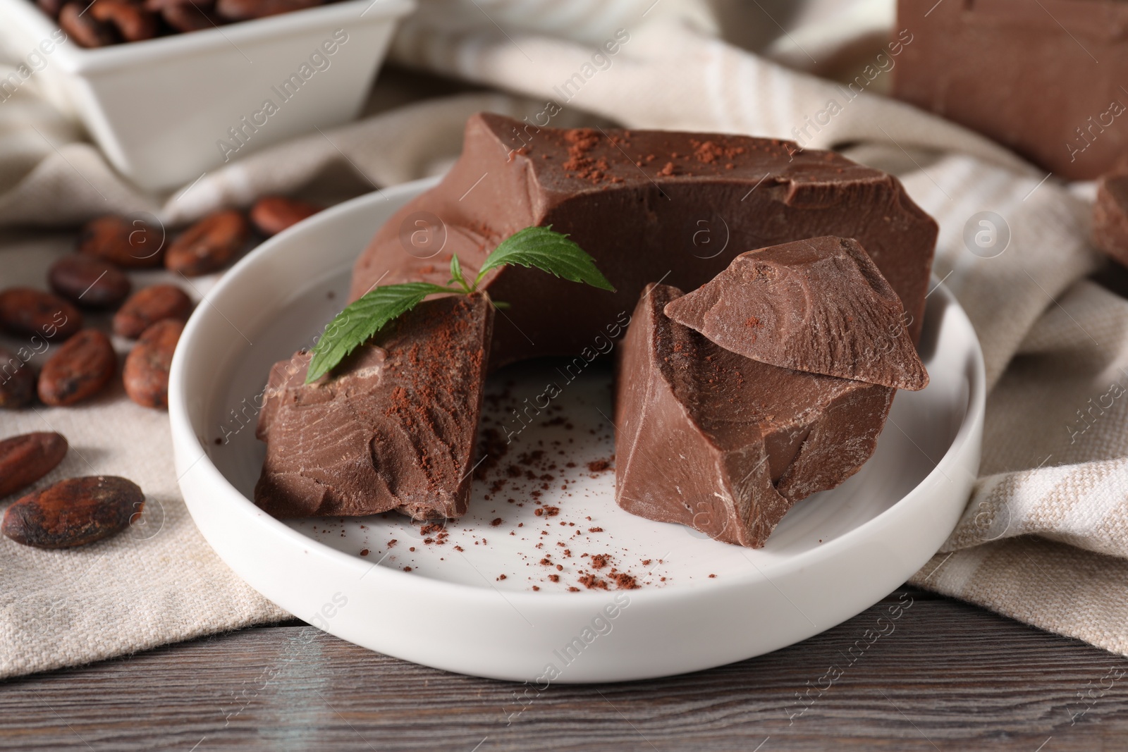 Photo of Pieces of tasty milk chocolate, cocoa beans, powder and mint on wooden table