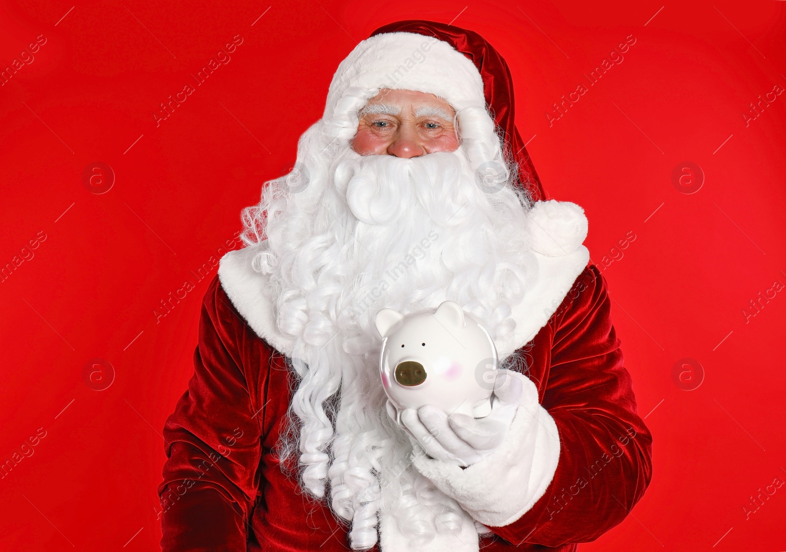 Photo of Santa Claus holding piggy bank on red background