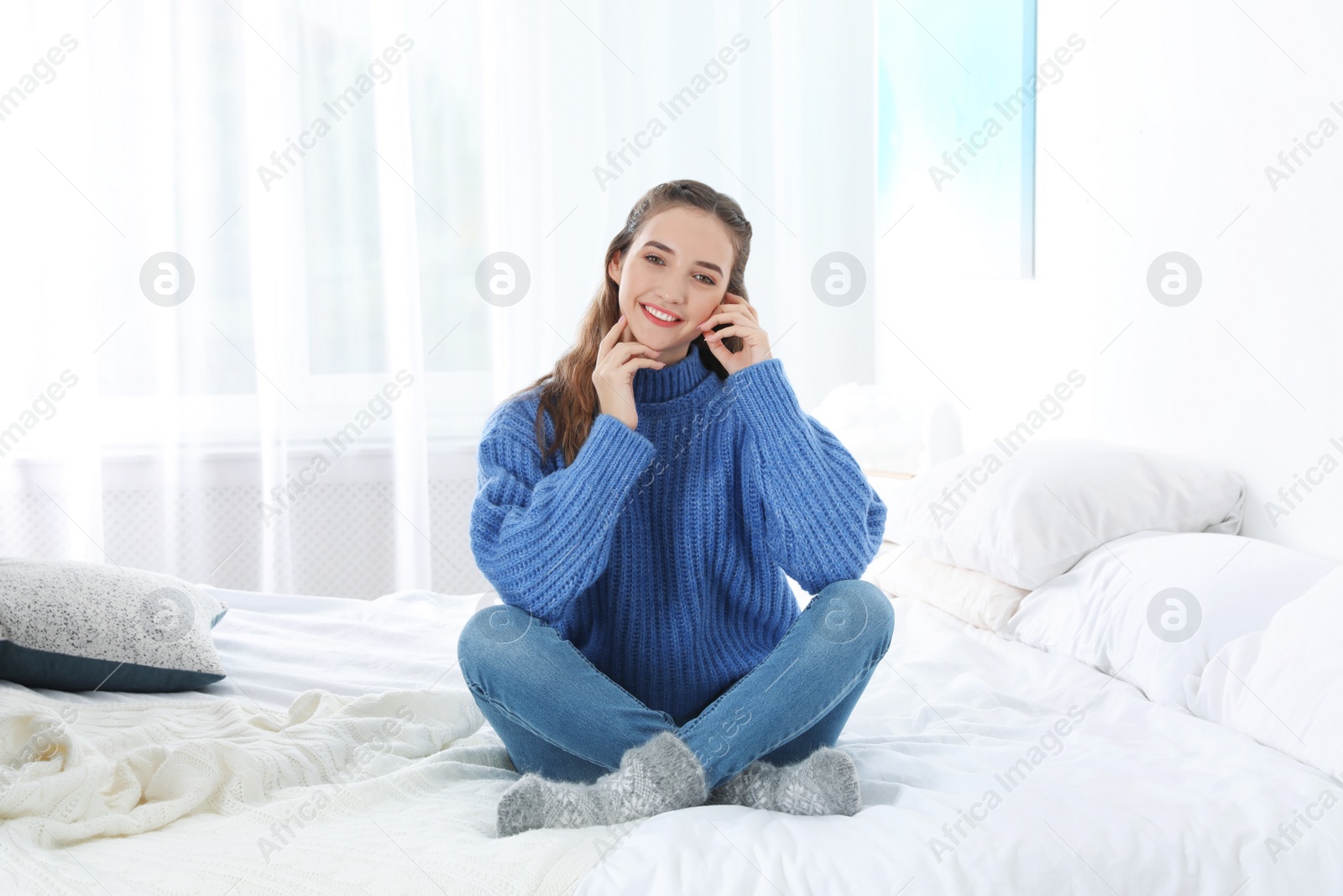 Photo of Beautiful teenage girl in warm cozy sweater on bed at home