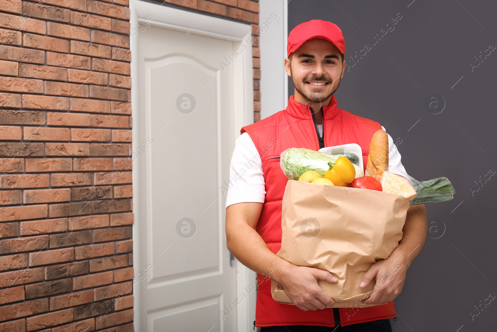 Photo of Food delivery courier holding paper bag with products indoors. Space for text