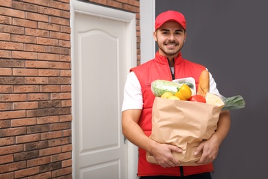 Food delivery courier holding paper bag with products indoors. Space for text