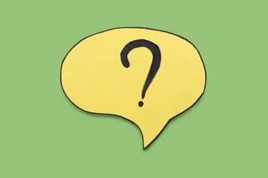 Paper speech bubble with question mark on green background, above view