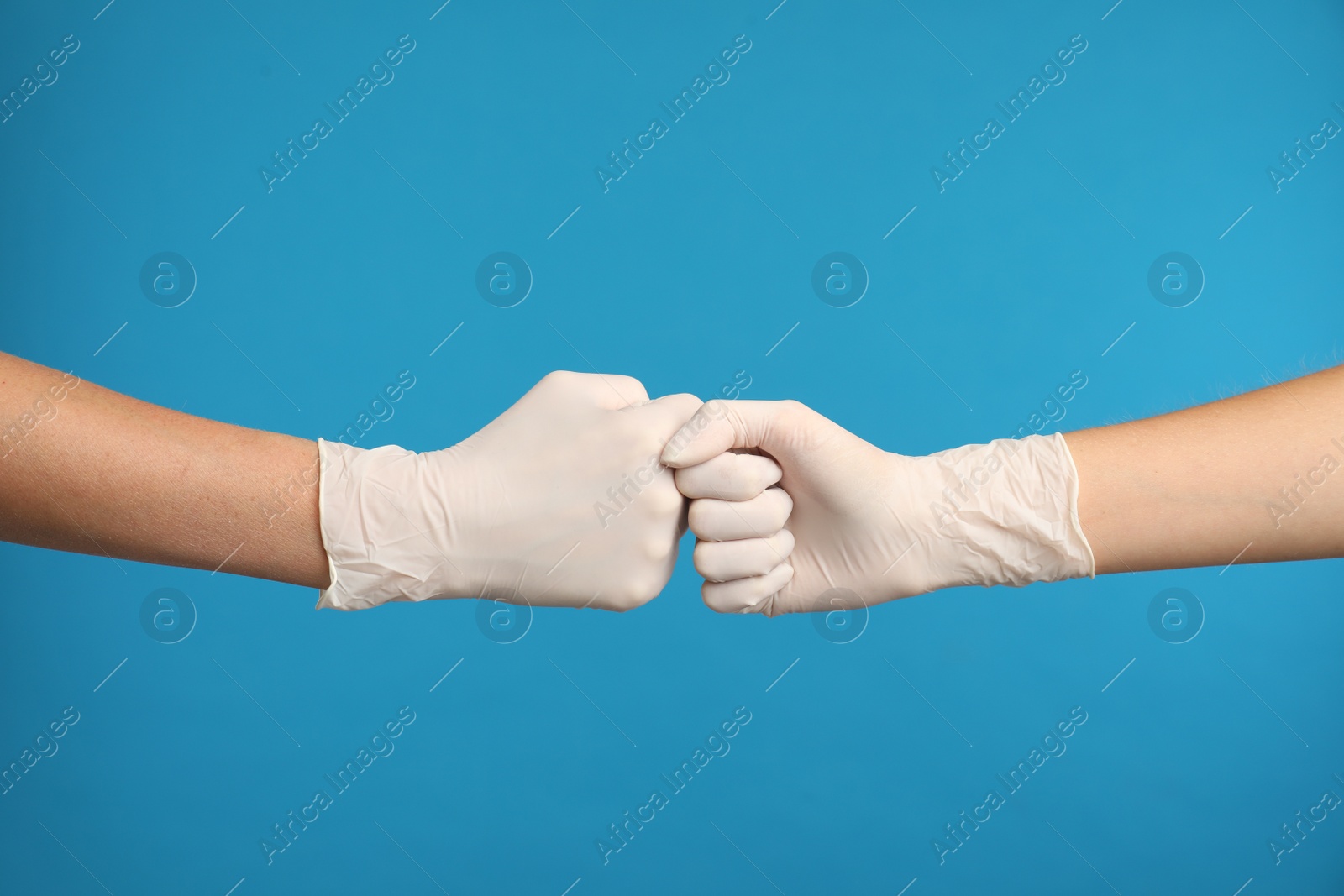 Photo of Doctors in medical gloves making fist bump on light blue background, closeup