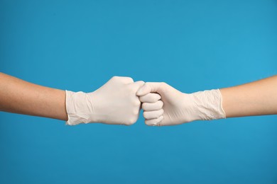 Photo of Doctors in medical gloves making fist bump on light blue background, closeup