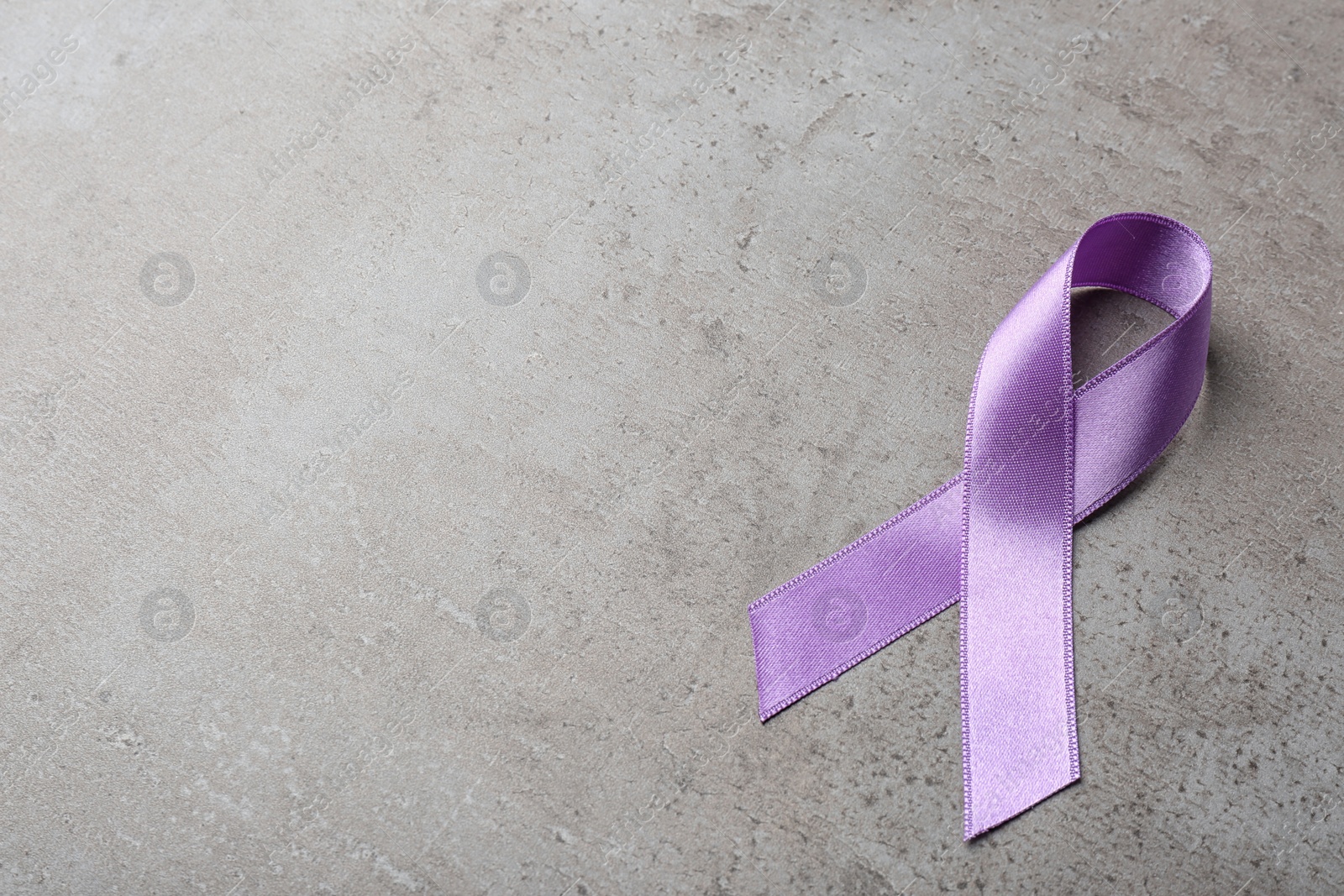 Photo of Purple ribbon on grey stone background, space for text. Domestic violence awareness