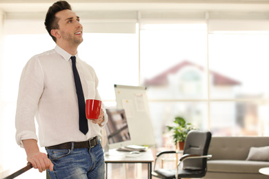 Young businessman with cup of drink relaxing in office during break