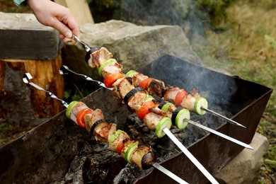 Woman cooking meat and vegetables on brazier outdoors, closeup