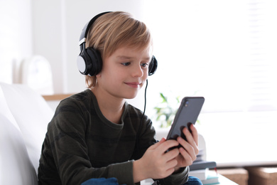 Cute little boy with headphones and smartphone listening to audiobook at home