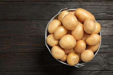 Photo of Raw fresh organic potatoes on black wooden background, top view. Space for text