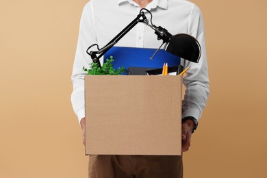 Photo of Unemployed young man with box of personal office belongings on beige background, closeup