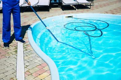Photo of Worker cleaning outdoor swimming pool with underwater vacuum, closeup
