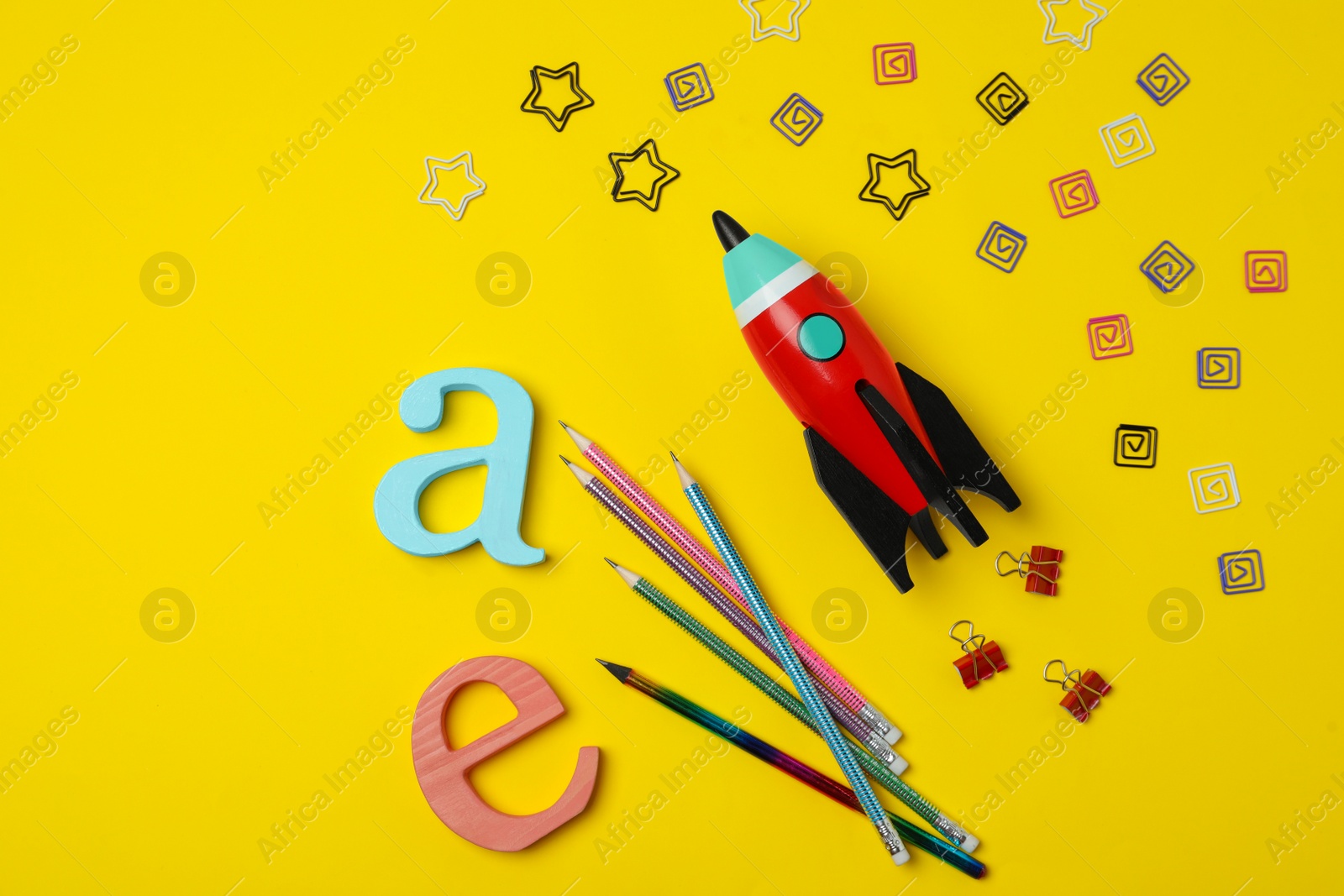 Photo of Bright toy rocket and school supplies on yellow background, flat lay. Space for text