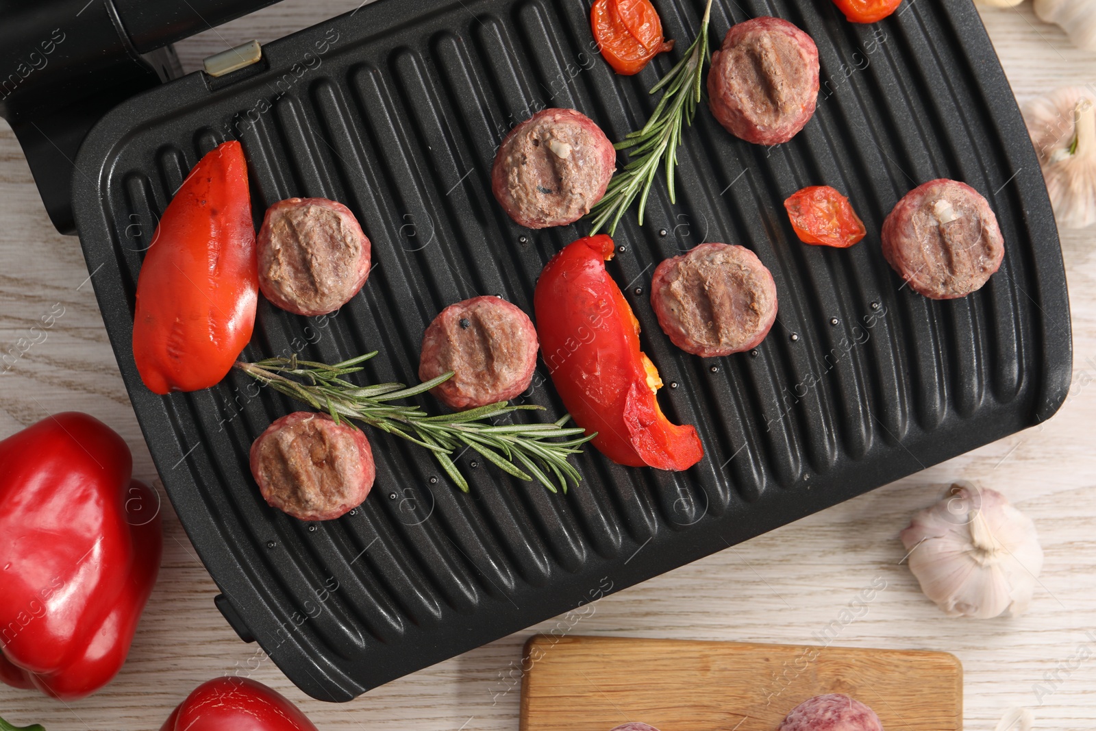 Photo of Electric grill with vegetables, meat balls and rosemary on wooden table, flat lay