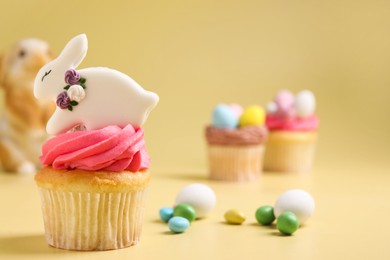 Photo of Tasty cupcakes with Easter decor on pale yellow background, closeup. Space for text