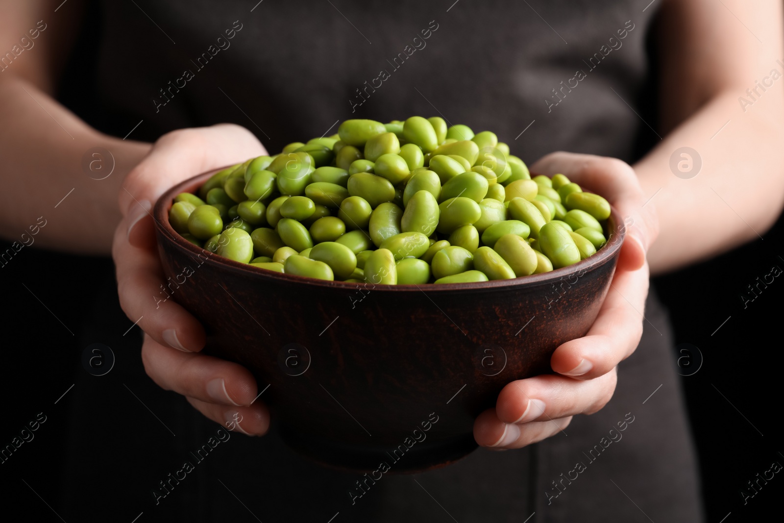 Photo of Woman holding bowl of edamame beans on dark background, closeup