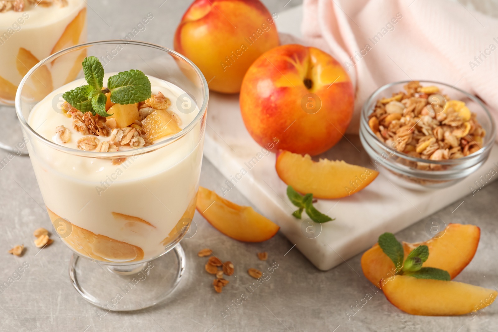 Photo of Tasty peach yogurt with granola, mint and pieces of fruits on light grey table