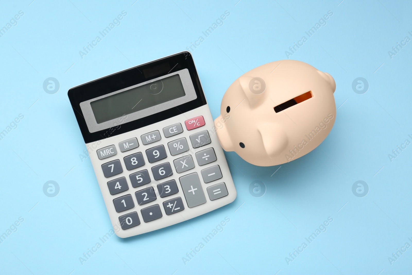 Photo of Calculator and piggy bank on light blue background, top view