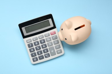 Calculator and piggy bank on light blue background, top view