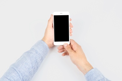 Photo of Young man holding mobile phone with blank screen in hands on white background